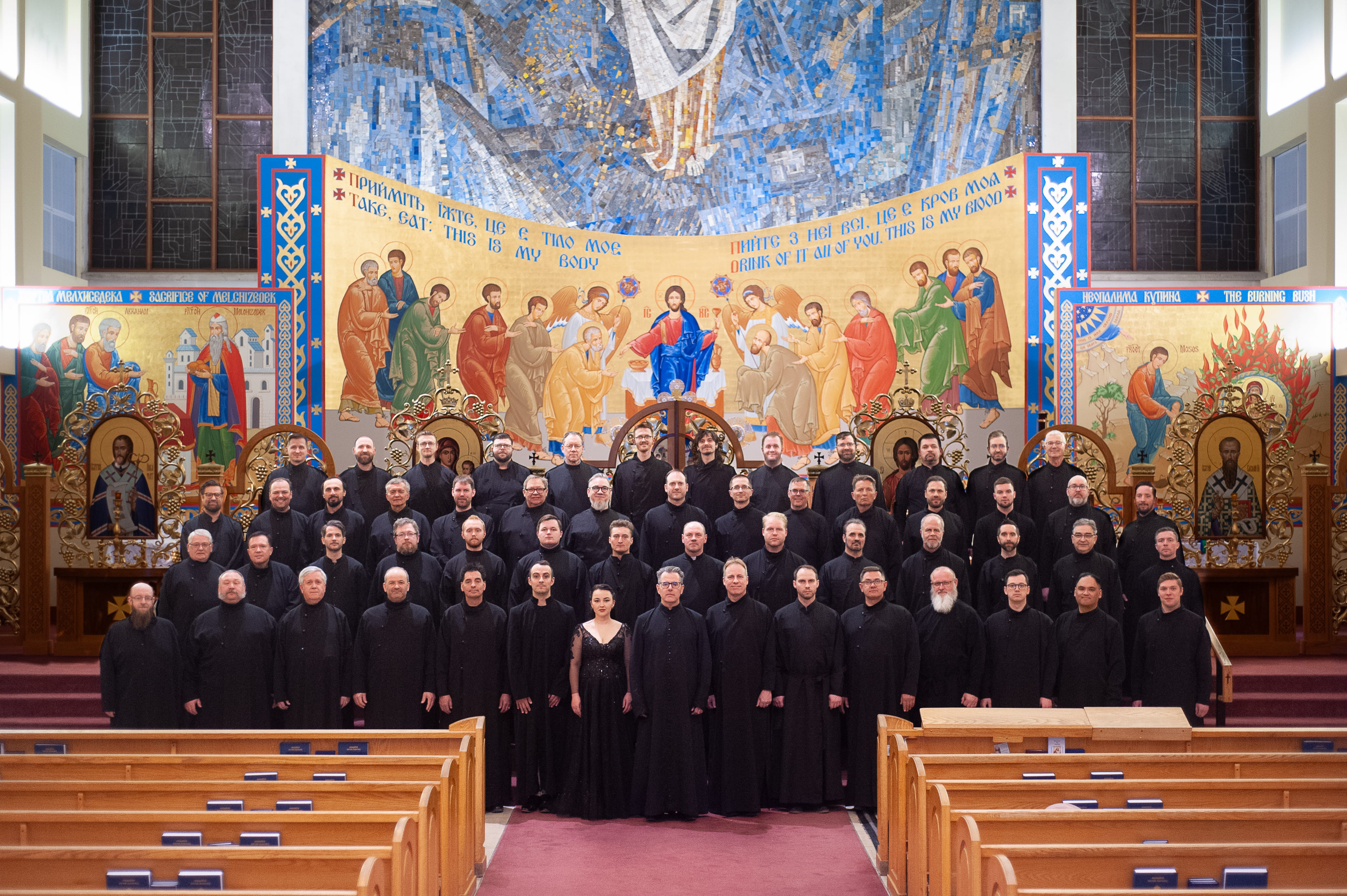 Axios Men's Ensemble gathered in front of an Eastern Christian mural.