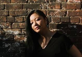 Vicky Chow poses by a brick wall. She wears a black dress.