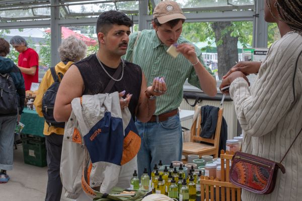two customers trying beauty products and engaging with a vendor at the farmers' market