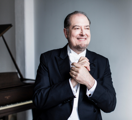 Garrick Ohlsson stands in a suit, clasping his hands.