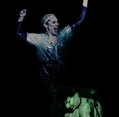 Two performers with stage make-up dance and pose on a black background