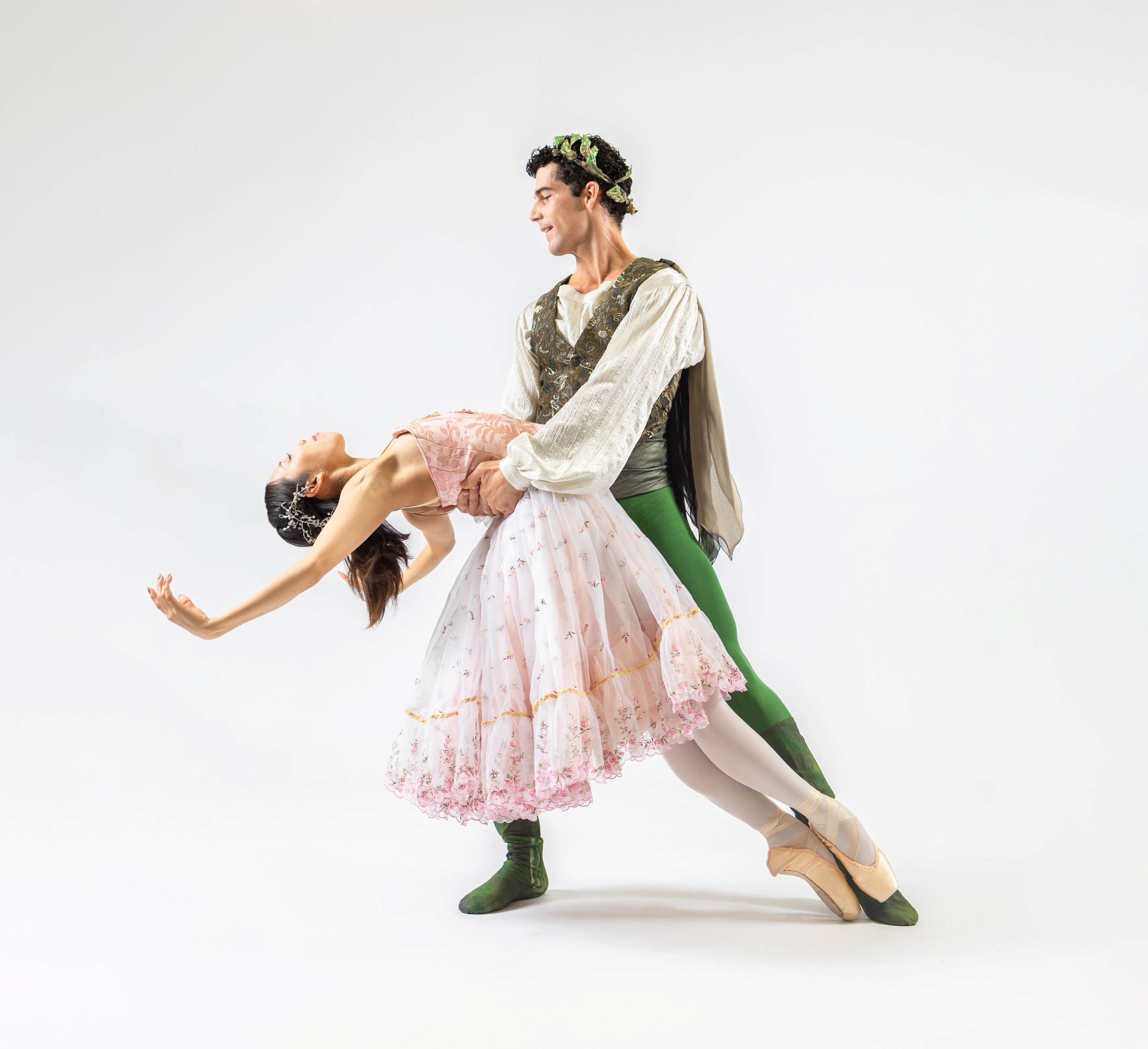 Two ballet dancers dressed in whimsical period clothing dancing against a white background.