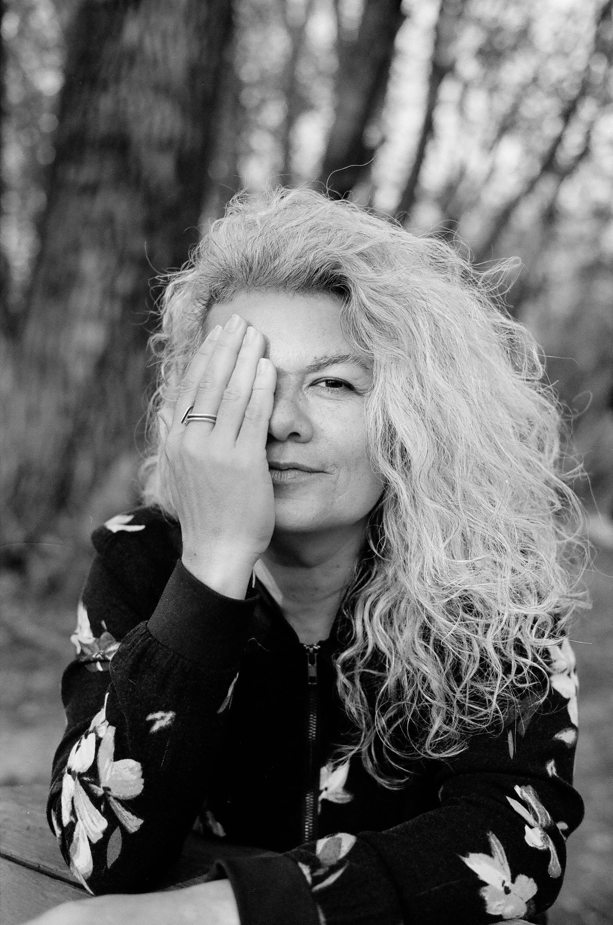 Mônica Freire. She covers half her face with one hand.