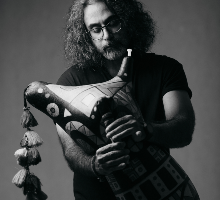 Mohsen Sharifan holds a unique instrument. He looks down towards it.