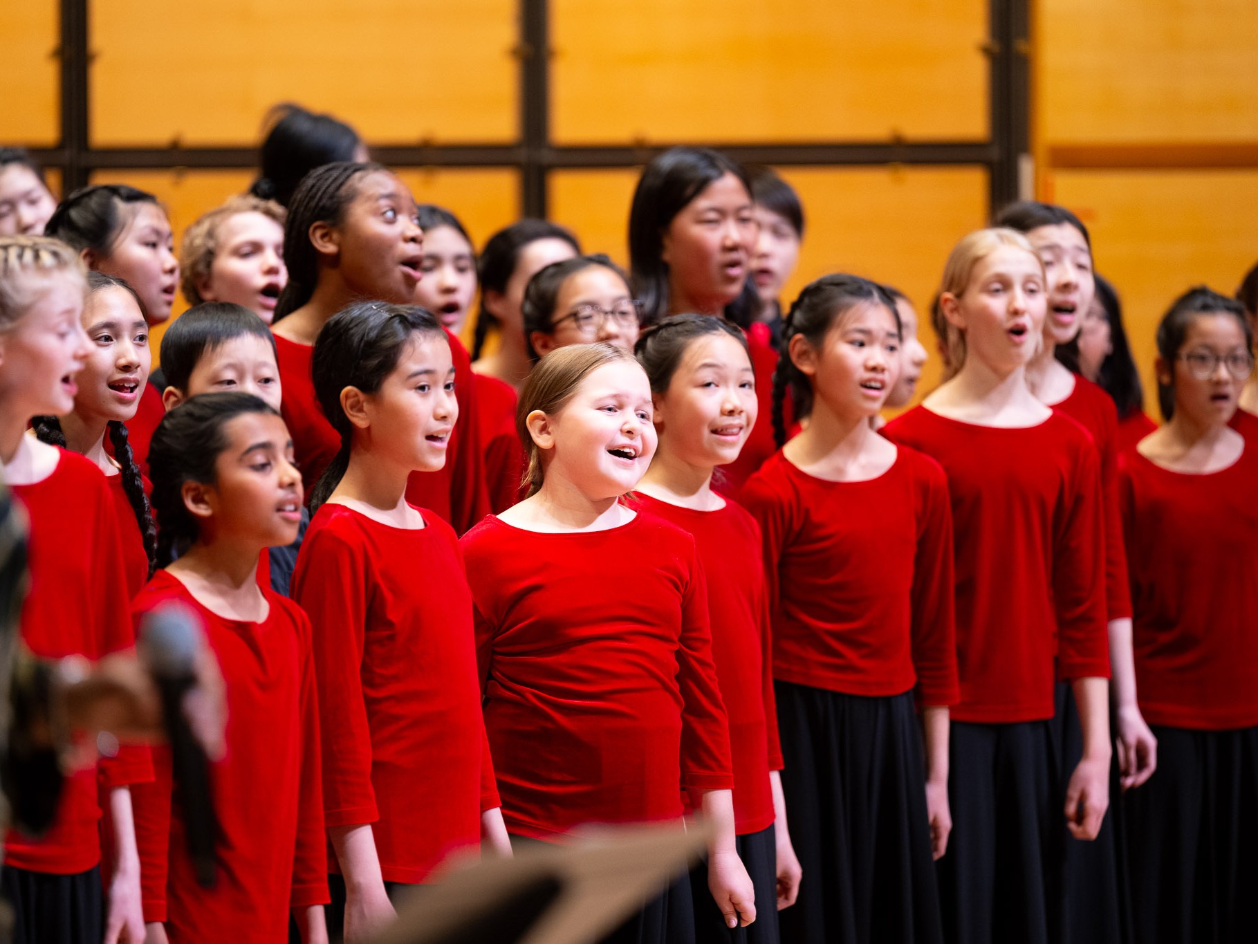 A children's choir  wearing red tops are singing on stage