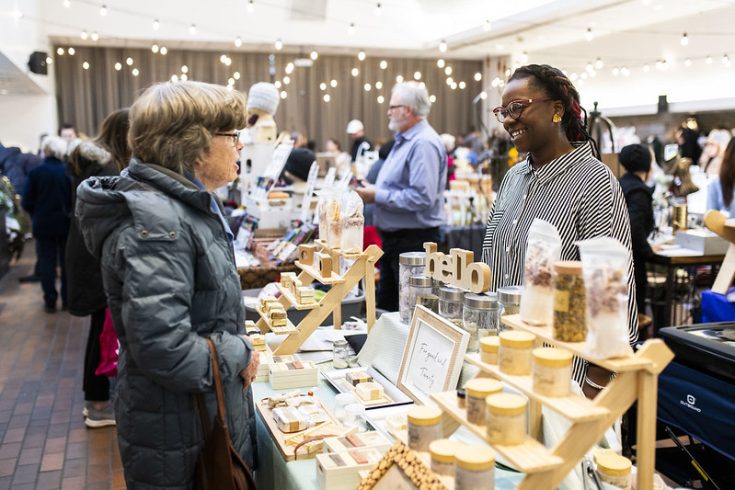 A person shopping at a lively holiday market, speaking with a vendor.