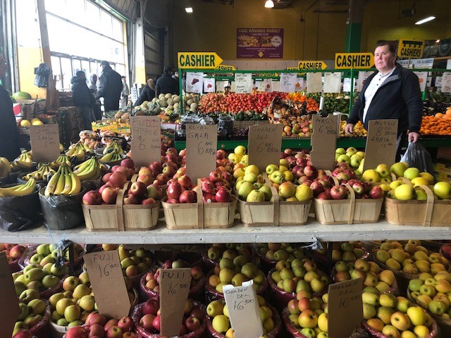 table with different types of apples in a display for sales, various signs in a busy market. Shopper