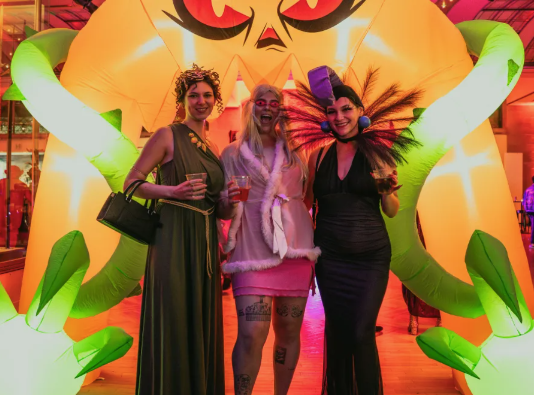Guests in costumes. They stand against an inflatable.