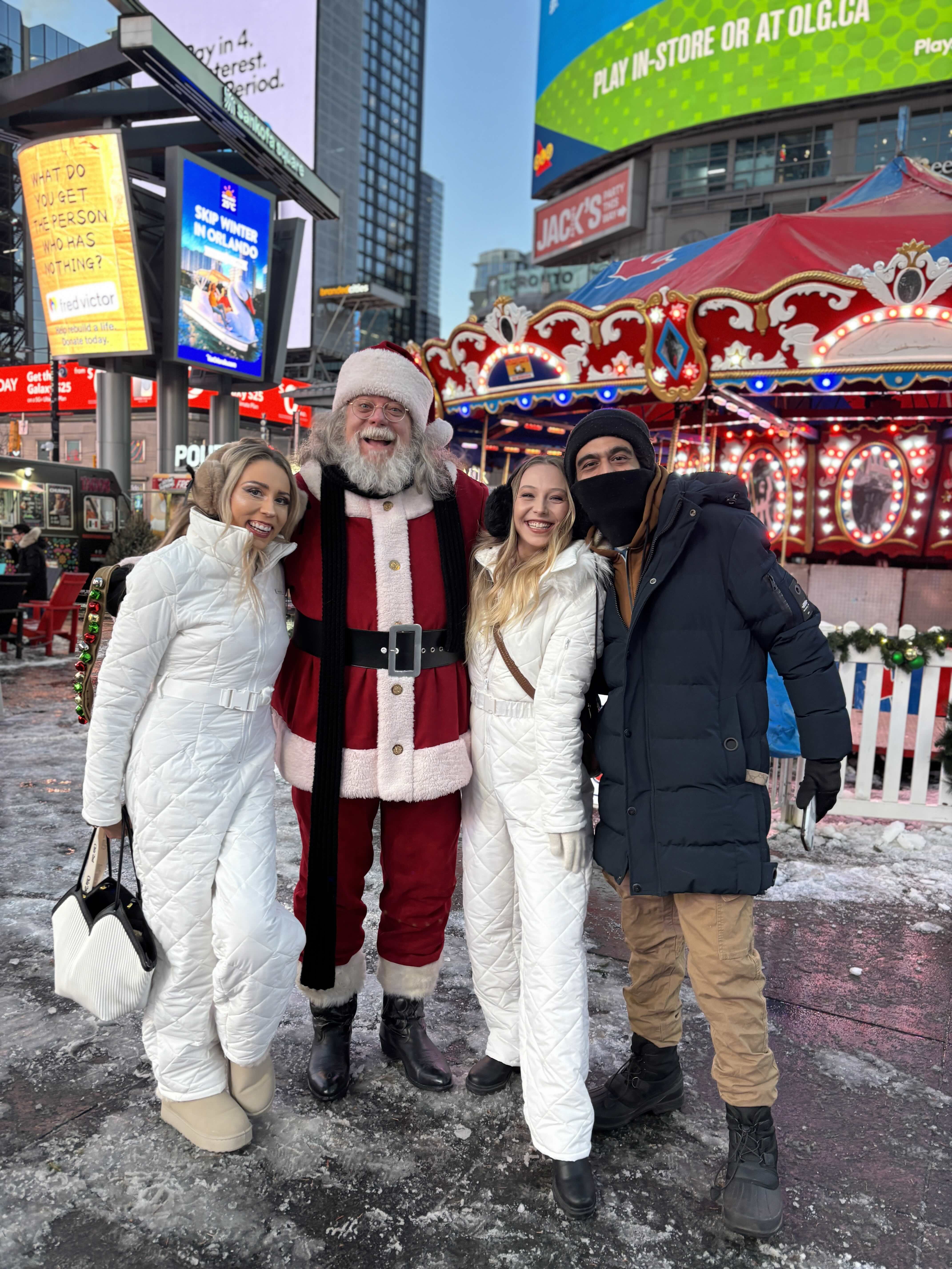 Santa Claus poses with three smiling adults dressed in winter coats at Toronto’s Holiday Fair in Sankofa Square.