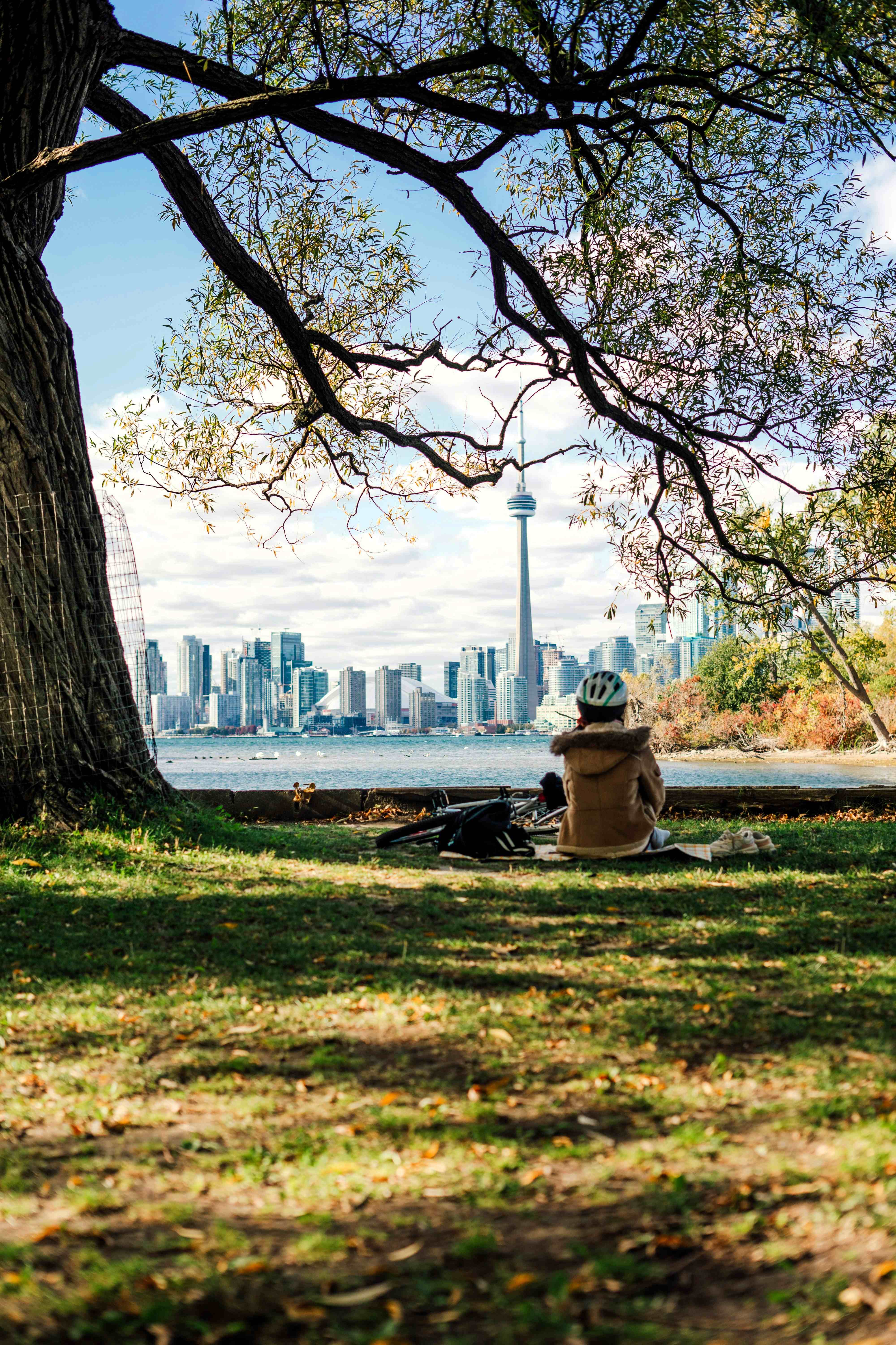 A woman sitting on Toronto Island in fall admiring the view of the city