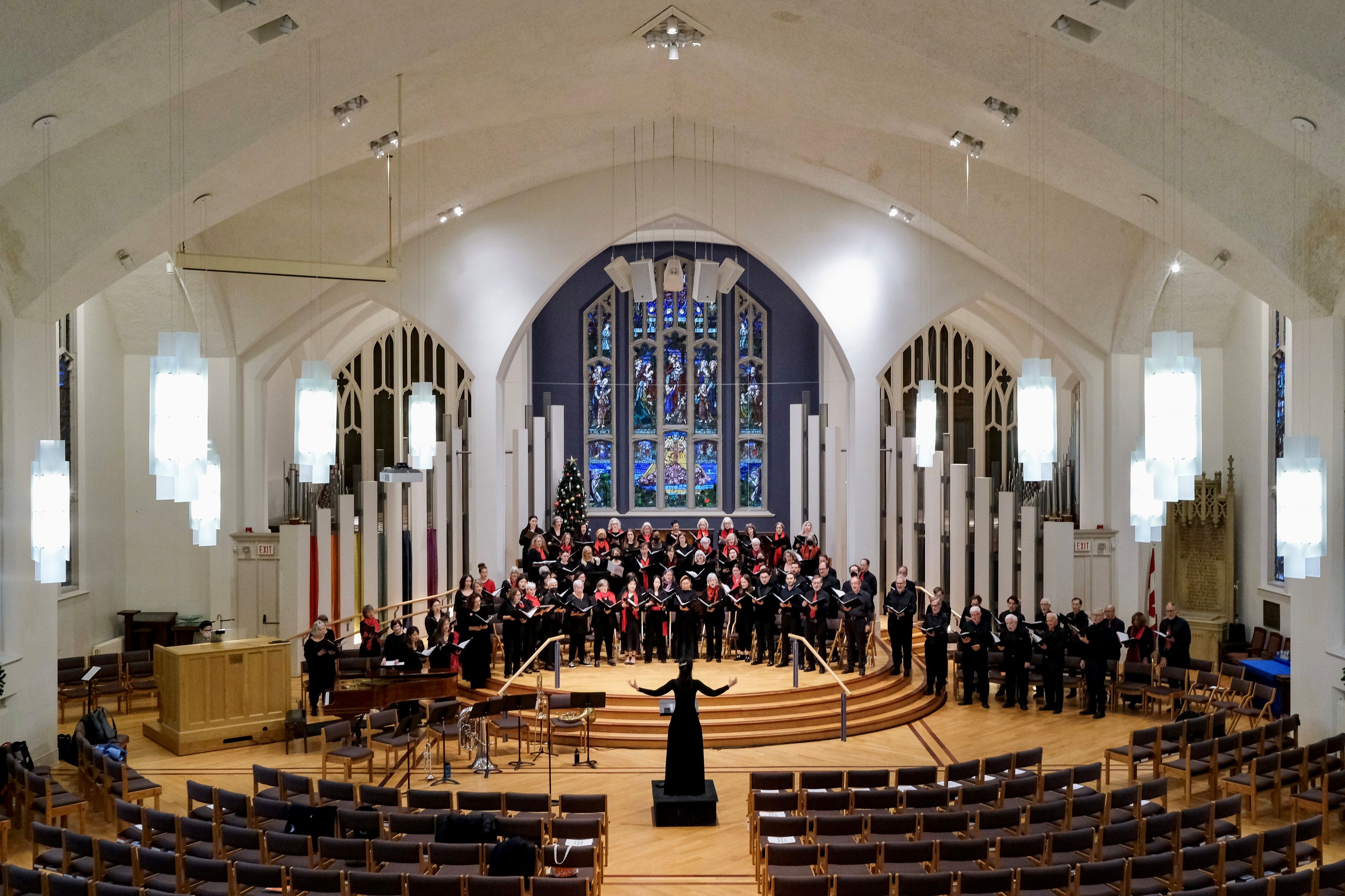 A concert hall with white arched ceilings, light brown floors and rows of black chairs. Orchestra of 40 people in black
