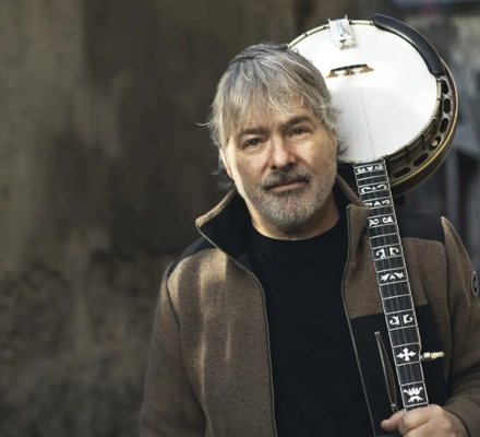 A man holds a banjo over his shoulder.