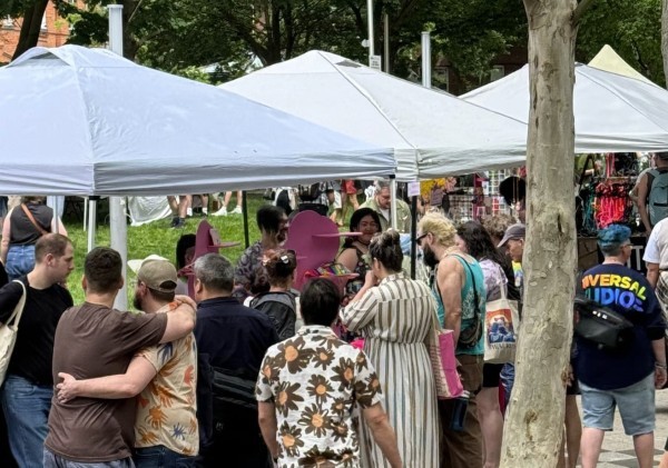 outdoor market with lots of customers. LGBTQ products. Two men hugging.
