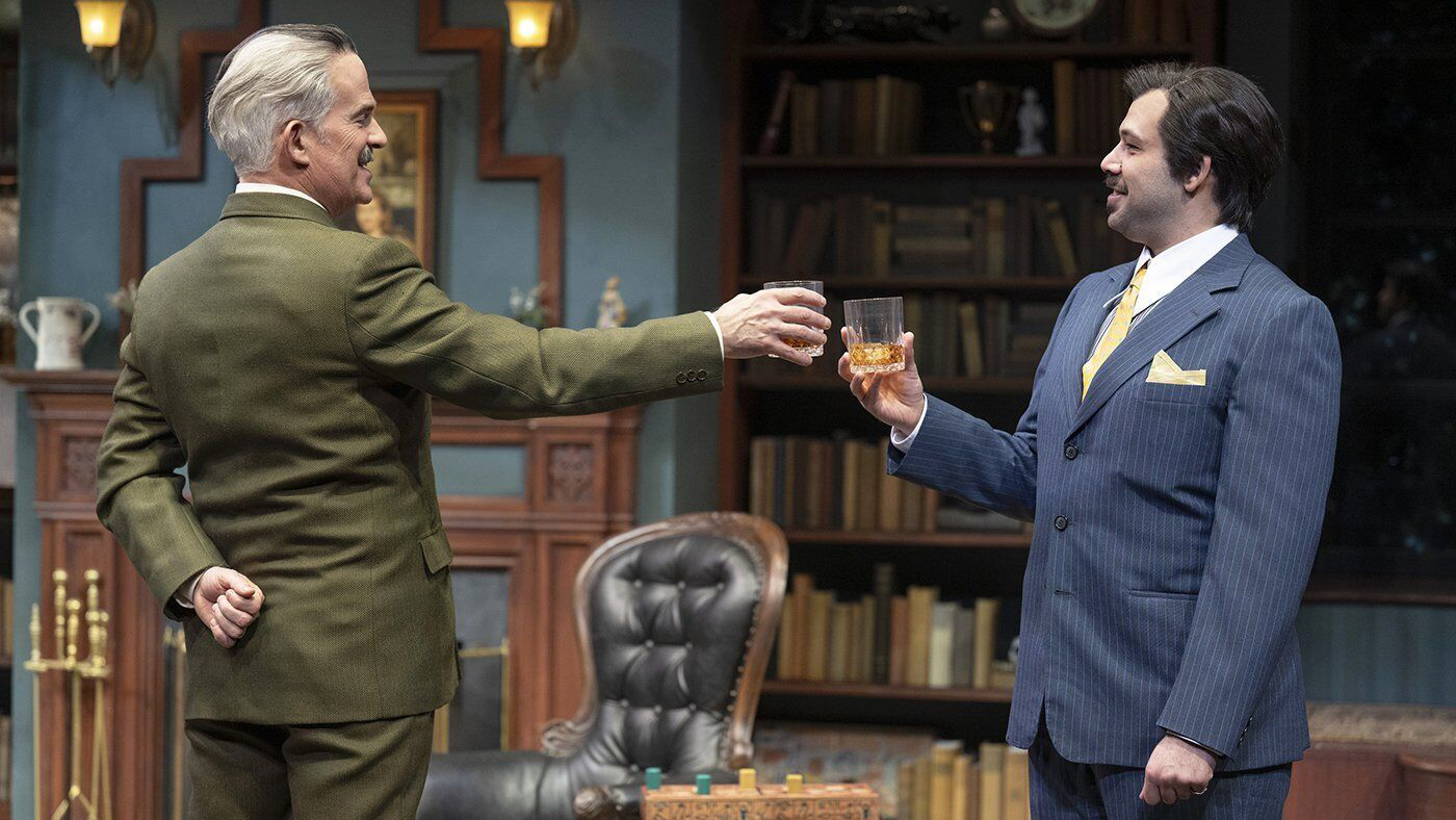 Two gentlemen cheers glasses of gin in a furnished living room, both in formal attire