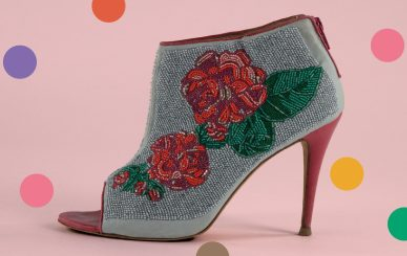 A beaded high heel rest on a pink background.