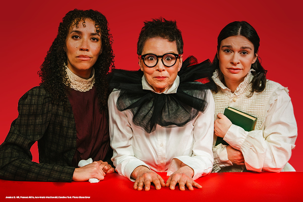 Three people posed behind a red table, styled in period-inspired costumes against a bold red backdrop.