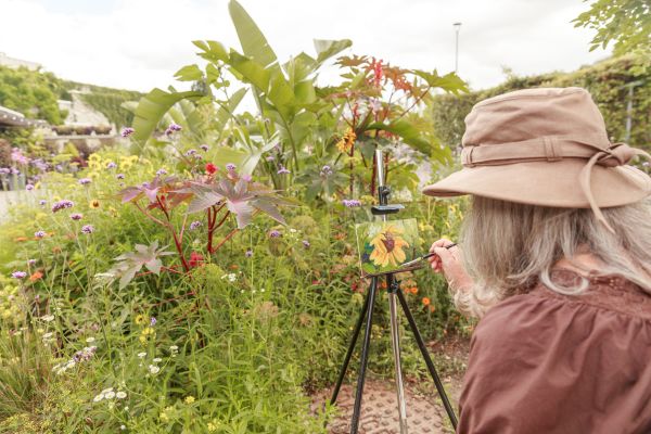 Artist painting a sunflower outside in a garden.