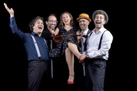 A group of men wearing suspenders, hoist a women up. She sits in a chair.