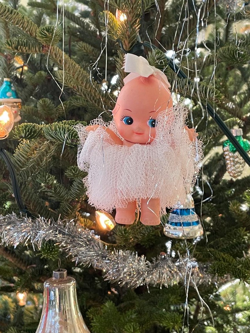 A rubber kewpie doll decoration on a tinsel covered pine tree.