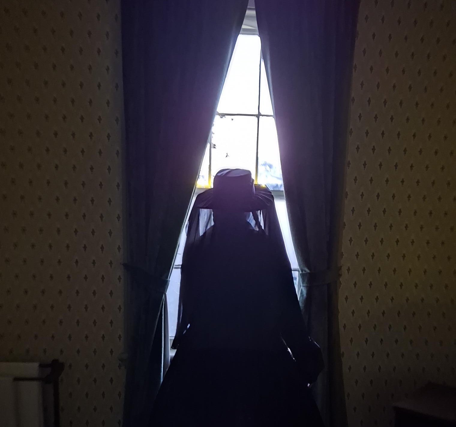 A person shrouded in black looking out a window.