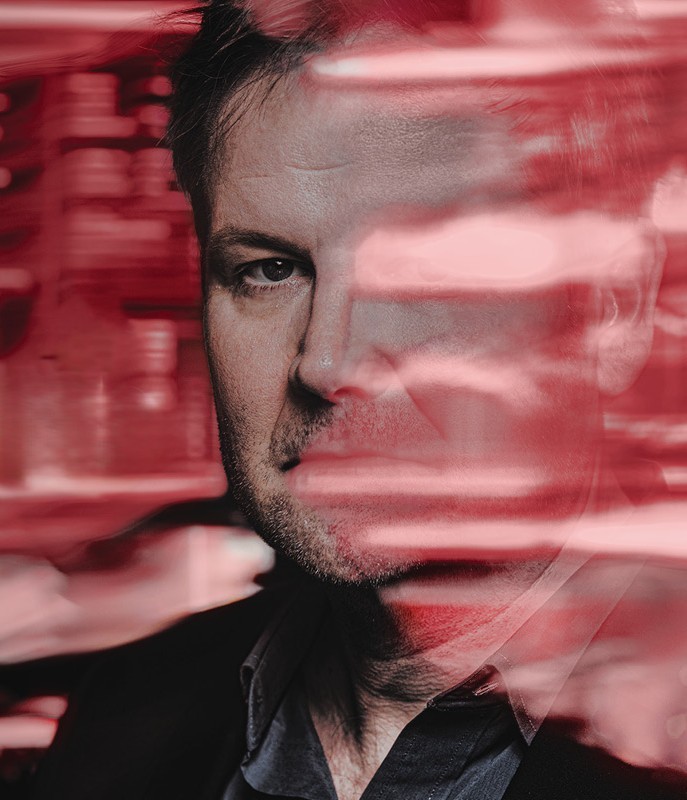 closeup of middle aged white man in black jacket, with his faced obscured and surrounded by red streaks of light