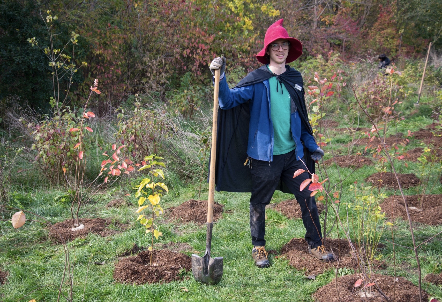 City staff wearing a wizard costume posing with newly planted trees and shrubs at Halloween planting event
