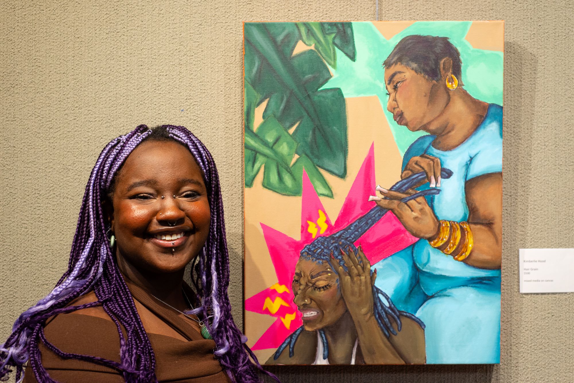 Artist Kimberlie Hood standing next to her painting of a woman doing another woman's hair.