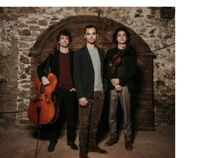 Three men stand under a brick archway holding string instruments.