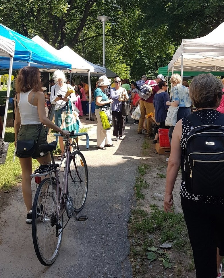Busy path in a park with vendor tents. Customer walking with a bike. Other customers shopping.