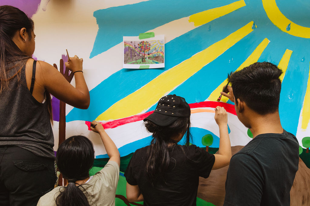 Four youth paint a colourful blue, yellow and magenta mural on a wall.